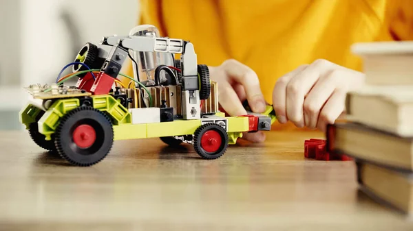 Cropped view of child playing with electric car made of building blocks on table near books — Stock Photo