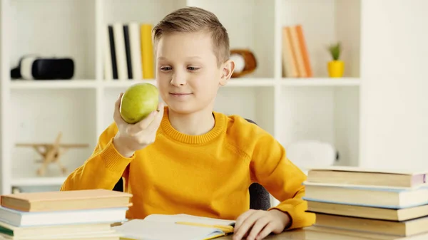 Schoolboy smiling while looking at green and tasty apple at home — Stock Photo