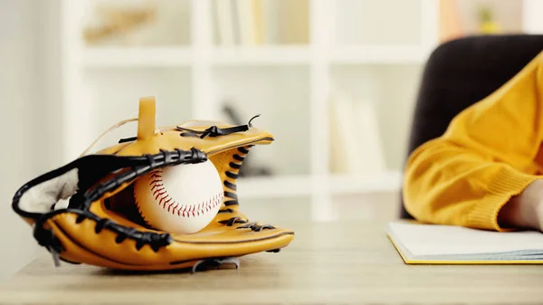 Baseball glove with ball near schoolkid doing homework at desk — Stockfoto