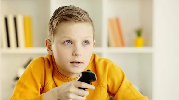 Boy with blue eyes looking away while playing video game at home — Stock Photo