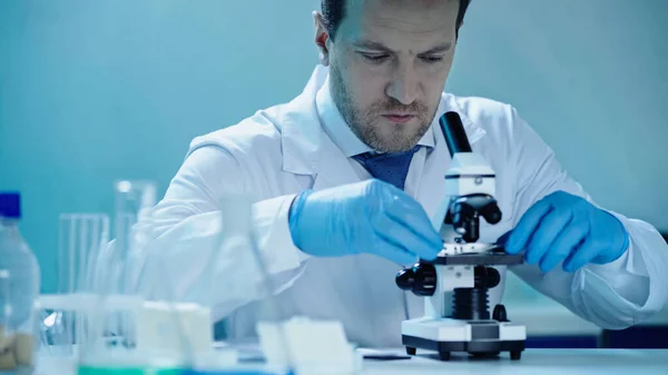 Вчений в латексі тримає зразок біля мікроскопа в медичній лабораторії — стокове фото