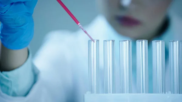 Partial view of blurred scientist adding red liquid into clean test tube in laboratory — стоковое фото