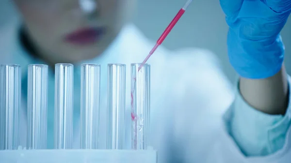 Частковий вигляд розмитого вченого, що додає червоний зразок у чисту пробірку в лабораторію — стокове фото