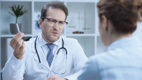 Serious doctor holding cigarette while talking to blurred patient in hospital — Stock Photo
