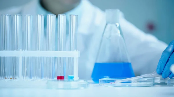 Partial view of blurred scientist in latex glove taking pipette on petri dish in laboratory — Stock Photo