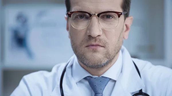 Confident doctor in glasses and white coat looking at camera in clinic — Stock Photo