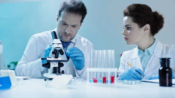 Вчений тримає скло зразком біля колеги в білому пальто, тримаючи олівець в лабораторії — стокове фото