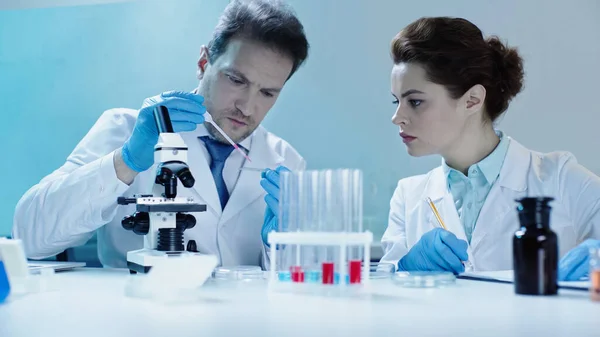 Scientist taking sample with pipette near colleague making notes in lab — Stock Photo