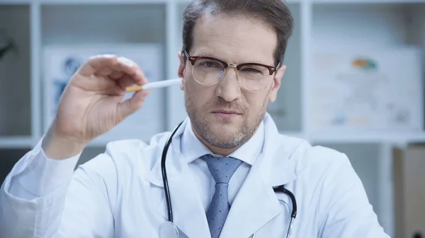 Serious doctor in glasses showing cigarette while looking at camera — Stock Photo