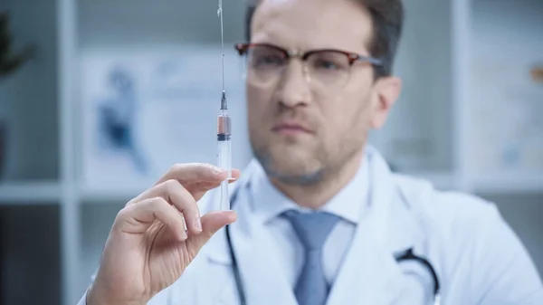 Blurred doctor in white coat and glasses holding syringe in clinic — Stock Photo
