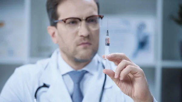 Serious doctor in white coat and glasses holding syringe in clinic — Stock Photo