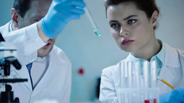 Два вчені в білих халатах дивляться на пробірку з вибіркою в лабораторії — стокове фото