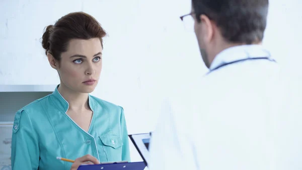 Лікар розмовляє з красивою медсестрою, що стоїть з буфером і пише діагноз — стокове фото