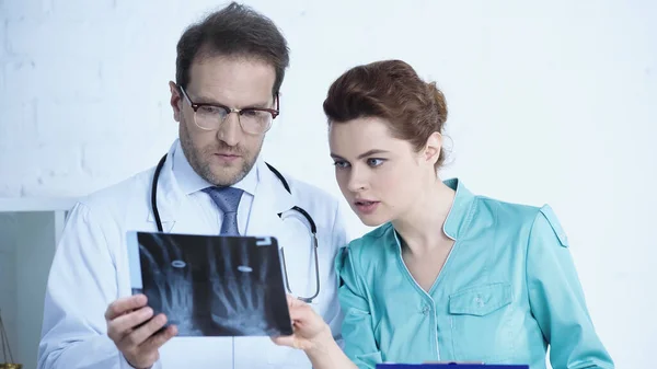 Pretty nurse looking at x-ray scan together with serious radiologist in clinic — Fotografia de Stock