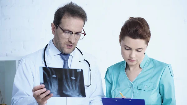 Radiologist holding x-ray while nurse writing on clipboard in clinic — Fotografia de Stock