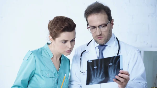 Nurse looking at x-ray scan together with serious radiologist in clinic — Stock Photo