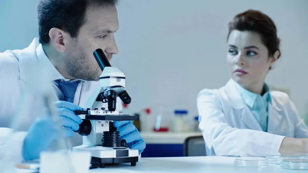 Scientist making analysis with microscope near pretty colleague sitting in laboratory — Stock Photo