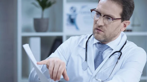 Serious cardiologist in glasses pointing with finger at cardiogram in hospital — Stock Photo