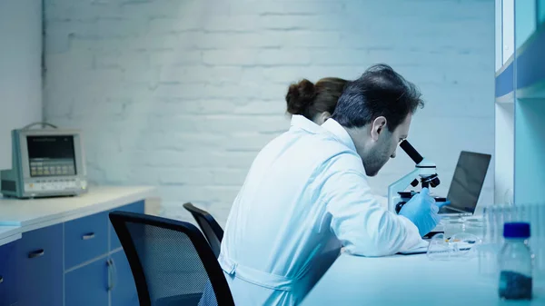 Two scientists making research near microscope and laptop in clinical laboratory - foto de stock