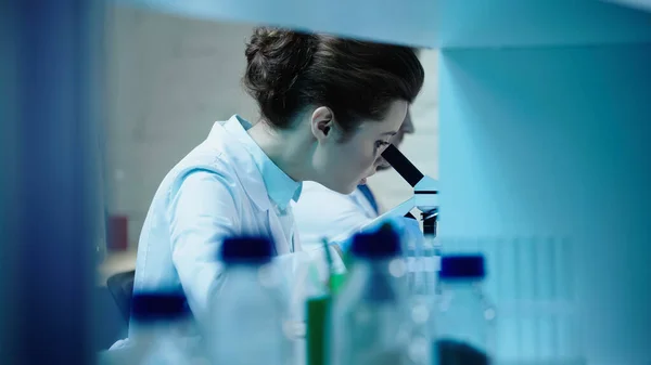 Scientist looking in microscope near blurred colleague in laboratory — Photo de stock