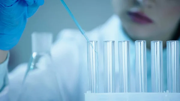 Частковий вид розмитого вченого, що додає блакитну рідину в чисту пробірку в лабораторії — стокове фото