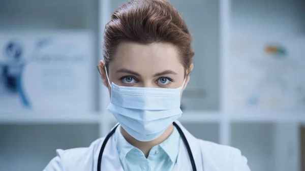 Female doctor in medical mask looking at camera in clinic — Stock Photo