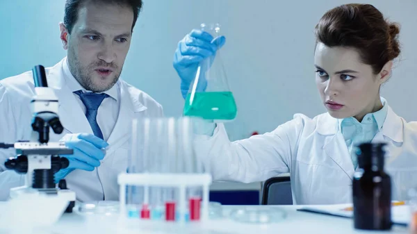 Scientist in white coat near colleague holding flask with liquid in laboratory — Stock Photo