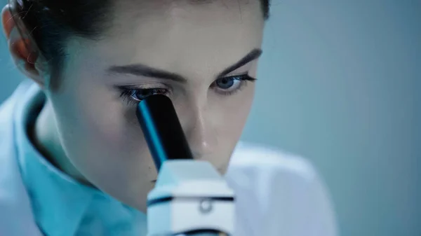 Крупним планом жінка-вчена, що дивиться через мікроскоп у клініці — стокове фото