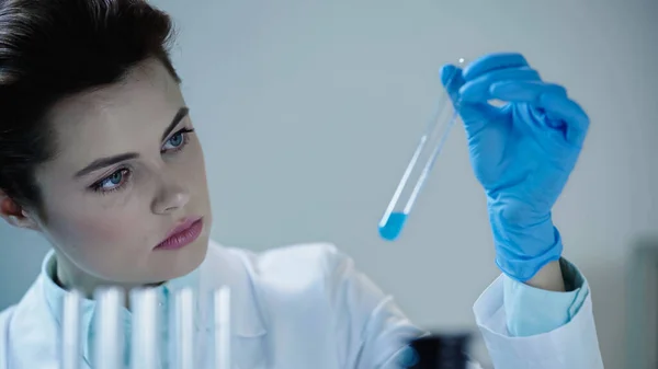 Attentive female scientist looking at blue liquid in test tube and writing down results — Stock Photo