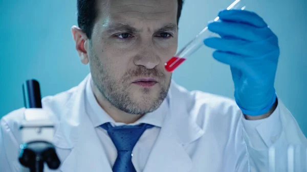 Чоловічий вчений дивиться на пробірку з червоною рідиною в клінічній лабораторії — стокове фото