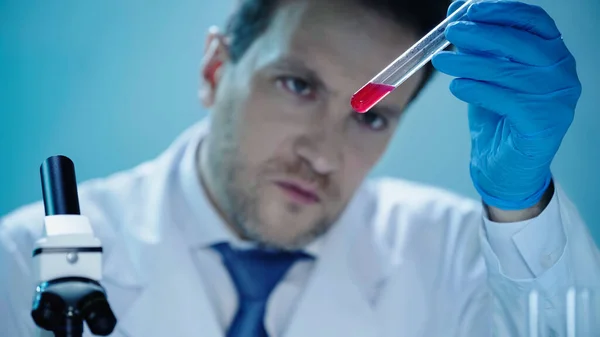 Серйозний вчений, дивлячись на пробірку з червоною рідиною в клінічній лабораторії — стокове фото