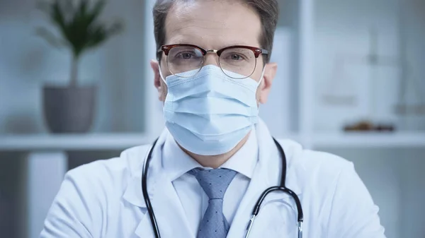 Doctor in glasses and medical mask looking at camera in clinic — стоковое фото