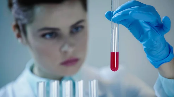 Жінка-вчена в латексній рукавичці тримає пробірку з червоною рідиною в лабораторії — стокове фото