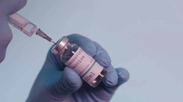 Cropped view of scientist in latex gloves filling in syringe with vaccine from bottle with lettering isolated on grey — стоковое фото