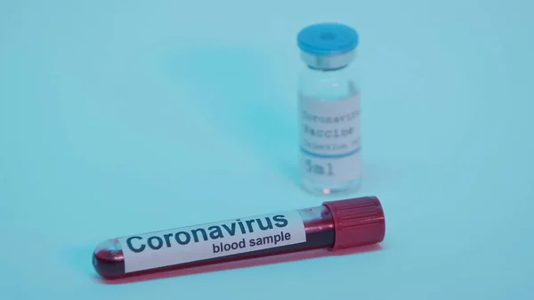 Blood sample in test tube with lettering and blurred bottle with coronavirus vaccine on blue — Stock Photo