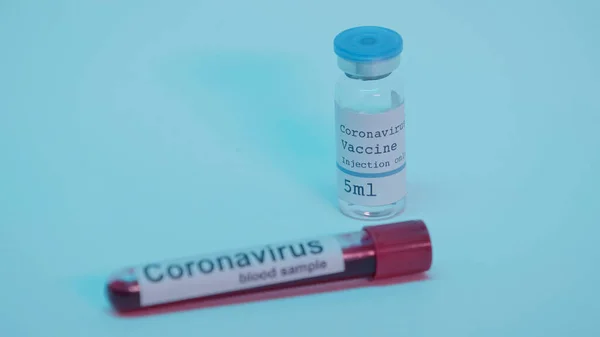 Sample with blood in test tube and bottle with coronavirus vaccine on blue - foto de stock