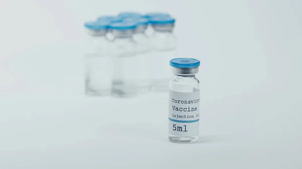 Glass bottle with coronavirus vaccine lettering with blurred background on white — Stock Photo