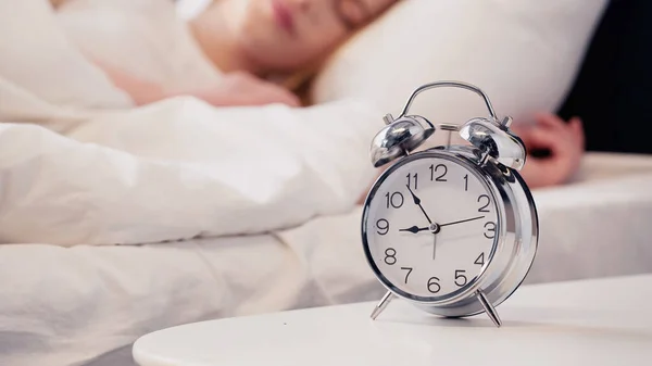 Cropped view of alarm clock on bedside table near blurred woman sleeping on bed — Stock Photo
