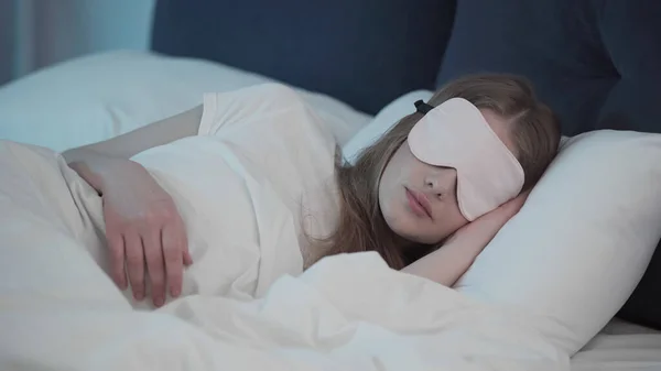 Young woman in sleep mask lying on bed at night — Stock Photo