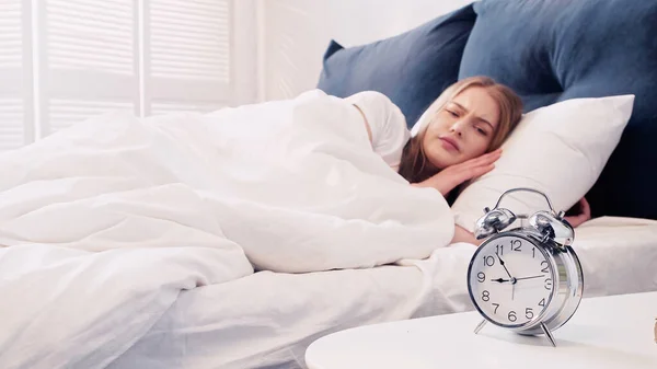 Sad woman looking at alarm clock on bedside table in bedroom — Stock Photo