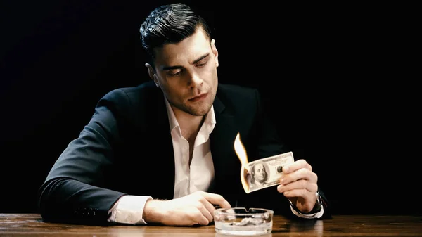 Бізнесмен у костюмі, що тримає банкноту горіння долара біля попільнички ізольовано на чорному — стокове фото