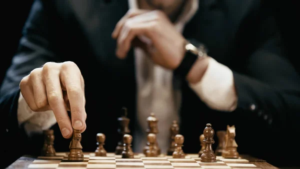 Cropped view of blurred businessman holding chess figure isolated on black — Stock Photo