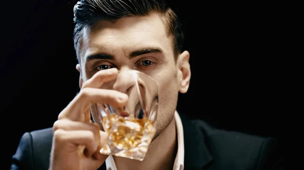 Businessman in formal wear holding glass and drinking whiskey isolated on black — стоковое фото