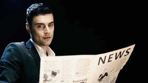 Businessman looking at camera near blurred newspaper isolated on black — Stock Photo