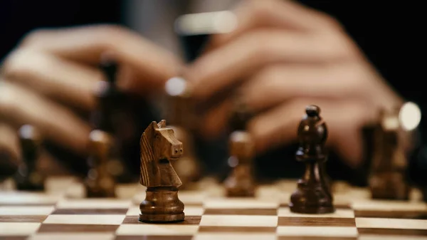 Cropped view of chess on board near blurred businessman isolated on black — Stock Photo