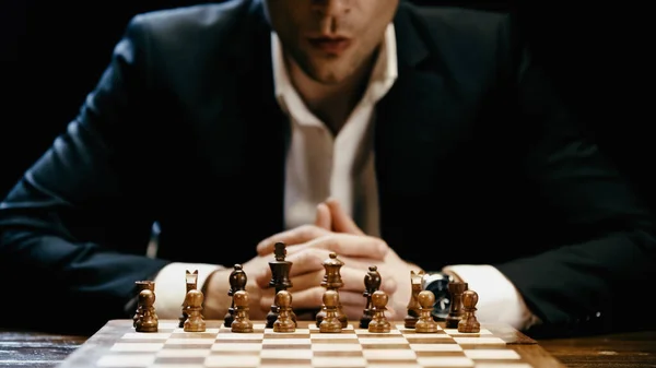 Cropped view of chess on board near blurred businessman in suit isolated on black — стоковое фото