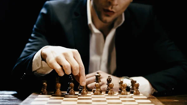 Cropped view of blurred businessman playing chess on table isolated on black - foto de stock