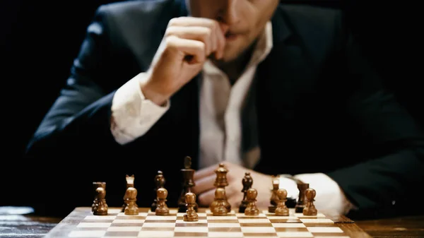 Cropped view of chess on board near blurred businessman at table isolated on black — Photo de stock