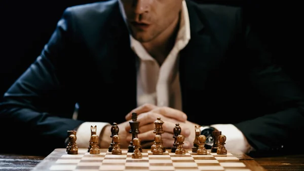 Cropped view of businessman sitting near chess on board isolated on black — Photo de stock