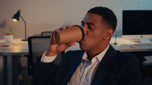 Gerente afroamericano en traje bebiendo café para ir a la oficina por la noche - foto de stock